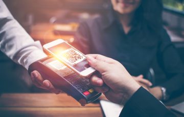 Young man hands are Smartphone to scan a QR CODE filing from a credit card reader to pay for food and beverages in restaurants which have a romantic atmosphere by the Asian girls are sitting together.